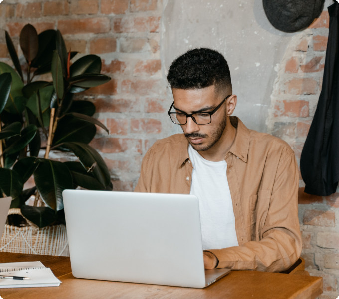 Person wearing glasses sits at a desk using a laptop, representing domain acquisition and management