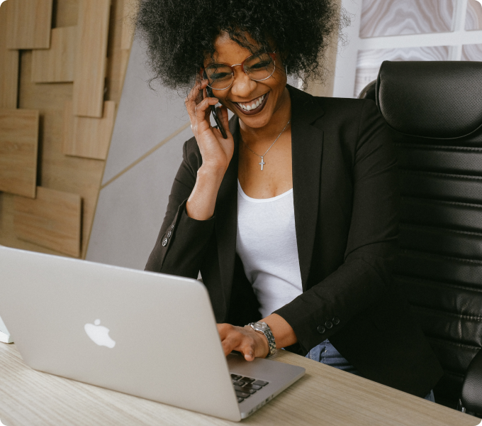 lady at desk using her laptop while on phone smiling