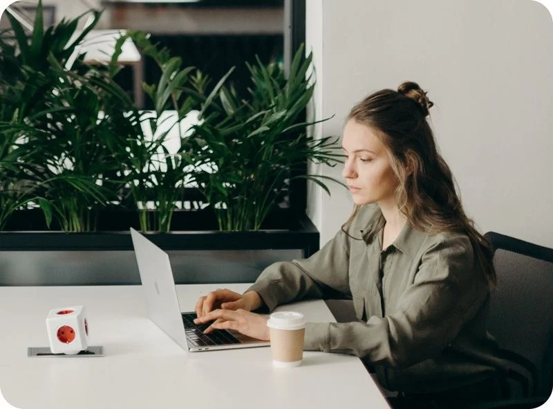 young lady at desk working on laptop with coffee and plants beside her